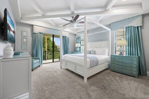 Quarto com cama de dossel, ventilador de teto, televisão e varanda com vista para o verde.