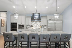 Una cocina moderna con una isla grande, electrodomésticos de acero inoxidable e iluminación colgante.