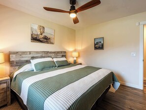 A bedroom with a wooden headboard, a bed with a striped green and white bedspread, a ceiling fan, and two wall-mounted lamps. - Diamond Grove- Pet Friendly- Mountain Chic (Red Lodge)