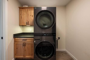 A compact laundry room with two stacked washing machines, wooden cabinets, and a countertop. - Diamond Grove- Pet Friendly- Mountain Chic (Red Lodge)