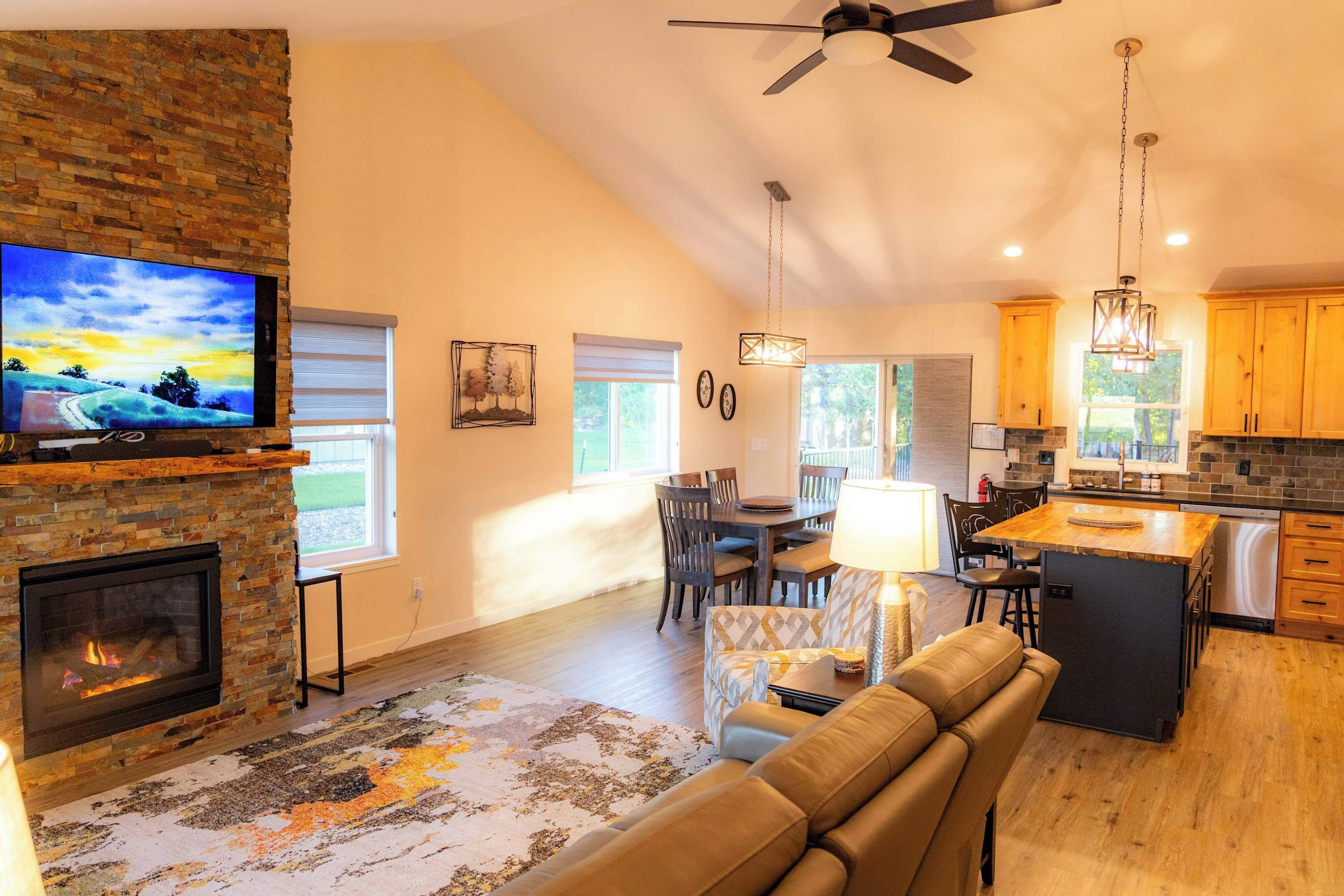 A modern kitchen with a stone fireplace, dining area with chairs, and a large TV mounted on the wall.