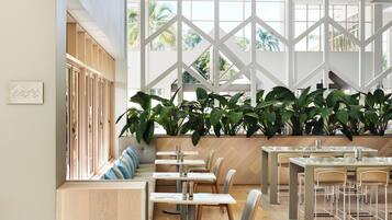 A modern restaurant interior with high ceilings, large windows, and a variety of seating arrangements including tables and benches.