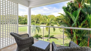 A balcony with wicker furniture, a glass table, and a view of a green landscape with trees and a clear sky. - Mirage Resort Villa 150 with access to Sheraton Facilities (Port Douglas)