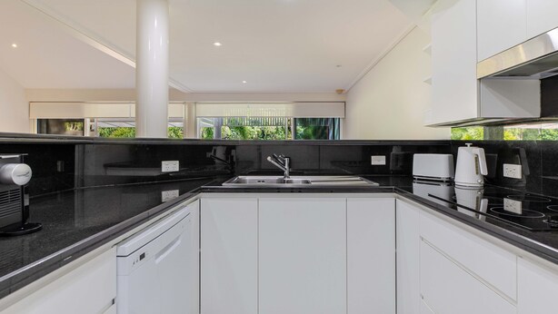 A modern kitchen with white cabinets, a black countertop, and stainless steel appliances. - Mirage Resort Villa 150 with access to Sheraton Facilities (Port Douglas)