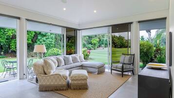 Un salon moderne avec un canapé d’angle, une table à manger et des chaises, de grandes fenêtres donnant sur un jardin luxuriant.