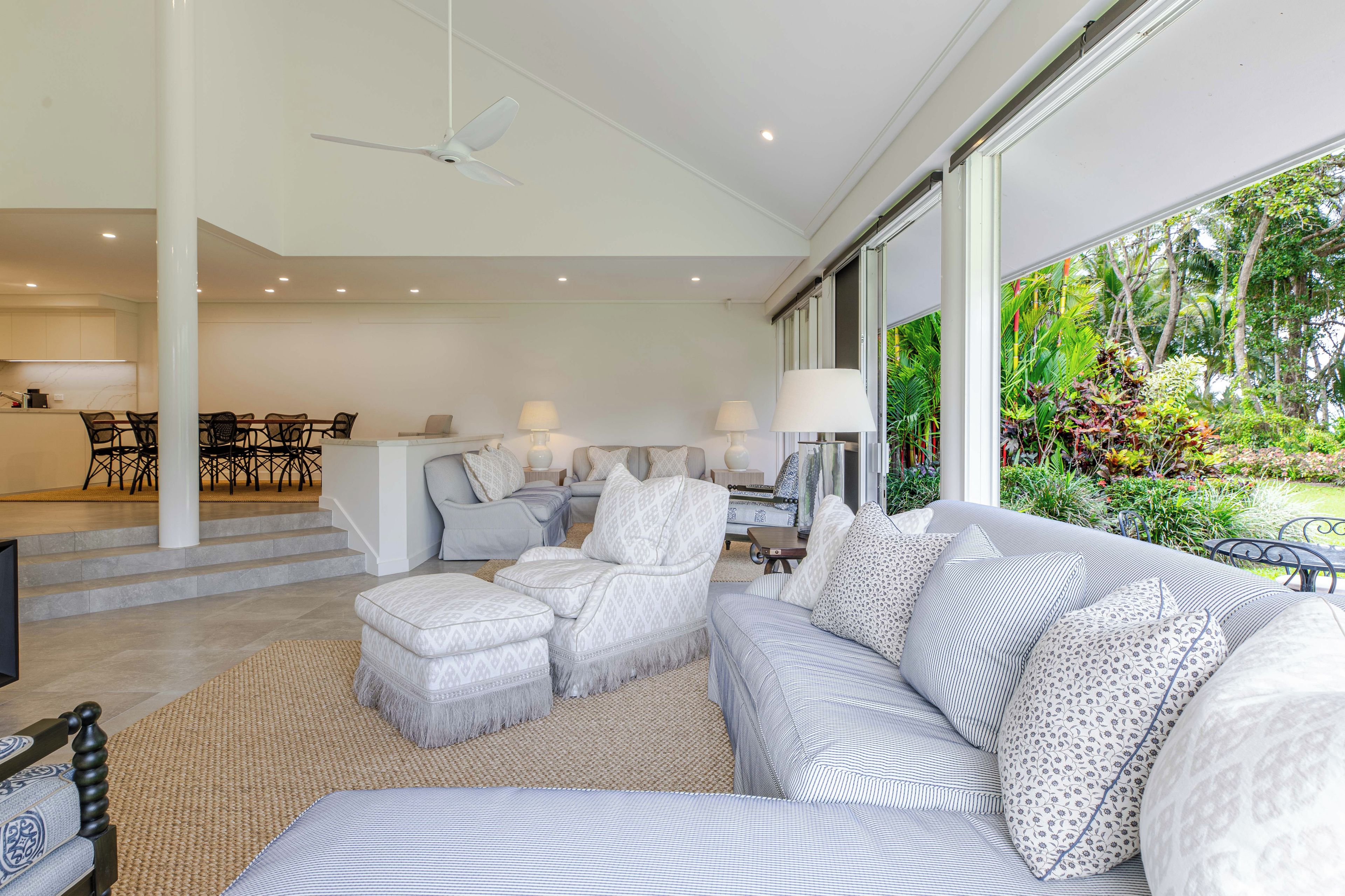 A modern living room with a sofa, ottomans, and a dining area with chairs and a table.