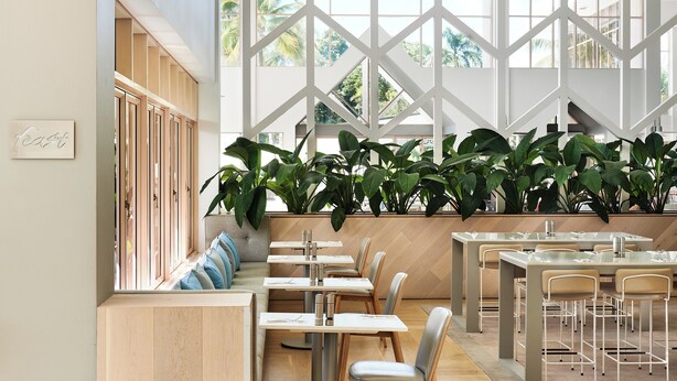 A modern restaurant interior with high ceilings, large windows, and a variety of seating arrangements including tables and benches. - Mirage Resort Villa 455 with access to Sheraton Facilities (Port Douglas)