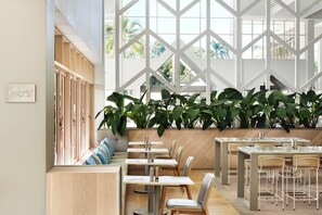 A modern restaurant interior with high ceilings, large windows, and a variety of seating arrangements including tables and benches.