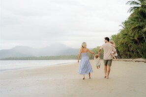 Eine Familie spaziert am Strand, im Hintergrund Palmen und Berge.