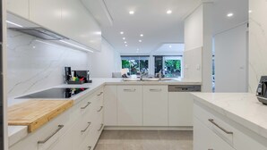 A modern kitchen with white cabinetry, a wooden countertop, and a built-in dishwasher. - Mirage Resort Villa 455 with access to Sheraton Facilities (Port Douglas)