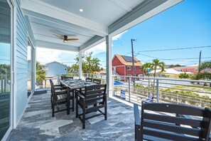 Eine überdachte Terrasse mit Tisch und Stühlen, einem Deckenventilator und Blick auf angrenzende Häuser.