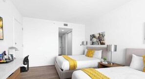 A hotel room with two beds, a desk with a chair, a lamp, and a painting on the wall. - Bay View Studio Beachwalk Elite Resort (Hallandale Beach)