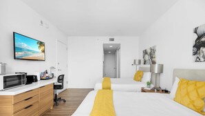Ein modernes Hotelzimmer mit einem Bett, Nachttischen, einem Schreibtisch mit Computer, einem Fernseher und Kunstwerken an den Wänden.
