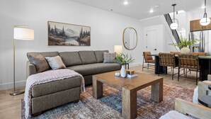 A modern living room with a sofa, coffee table, and dining area with chairs and a plant.