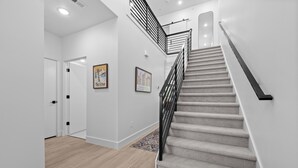 A modern staircase with a carpeted handrail, a wooden floor, and a white wall with framed pictures.