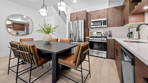 A modern kitchen with stainless steel appliances, a dining table with chairs, and a large mirror on the wall.