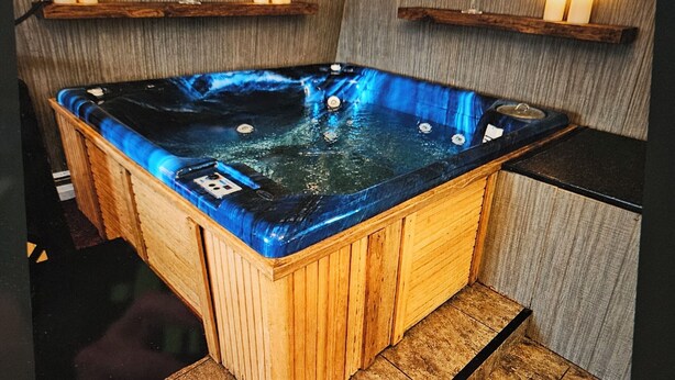 Una bañera de hidromasaje de madera con acabado azul, rodeada de paredes y estantes de madera con velas y copas.