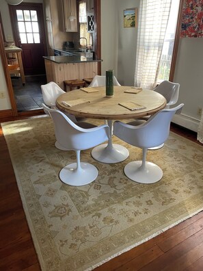 A dining area with a round wooden table surrounded by white chairs, a patterned rug, and a kitchen in the background. - Beautiful Ocean Grove Summer & Off-Season Rental (Neptune Township)