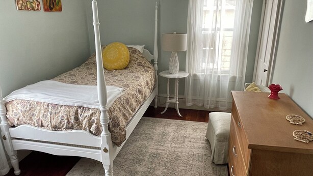 Um quarto com cama de dossel, mesa de cabeceira, abajur, cômoda e uma janela com cortinas.
