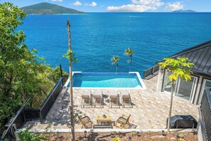 Ein Pool mit Liegestühlen und einem Tisch, mit Blick auf ein großes Gewässer und eine entfernte Insel.