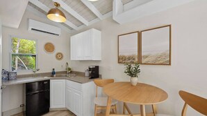 A kitchen with white cabinets, a black dishwasher, a wooden dining table with chairs, and two framed pictures on the wall. - The Parrot's Perch- New 6 BDRM Oceanfront Estate with Pool/Playground/Firepit (Lovenlund)