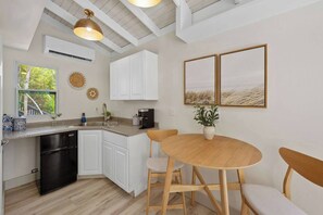 Eine Küche mit weißen Schränken, einem schwarzen Geschirrspüler, einem Holzespeisetisch mit Stühlen und zwei gerahmten Bildern an der Wand.