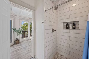 Ein Badezimmer mit weißen Fliesen im U-Bahn-Stil, einer Dusche mit Regendusche und einem Ablagebereich für Toilettenartikel.