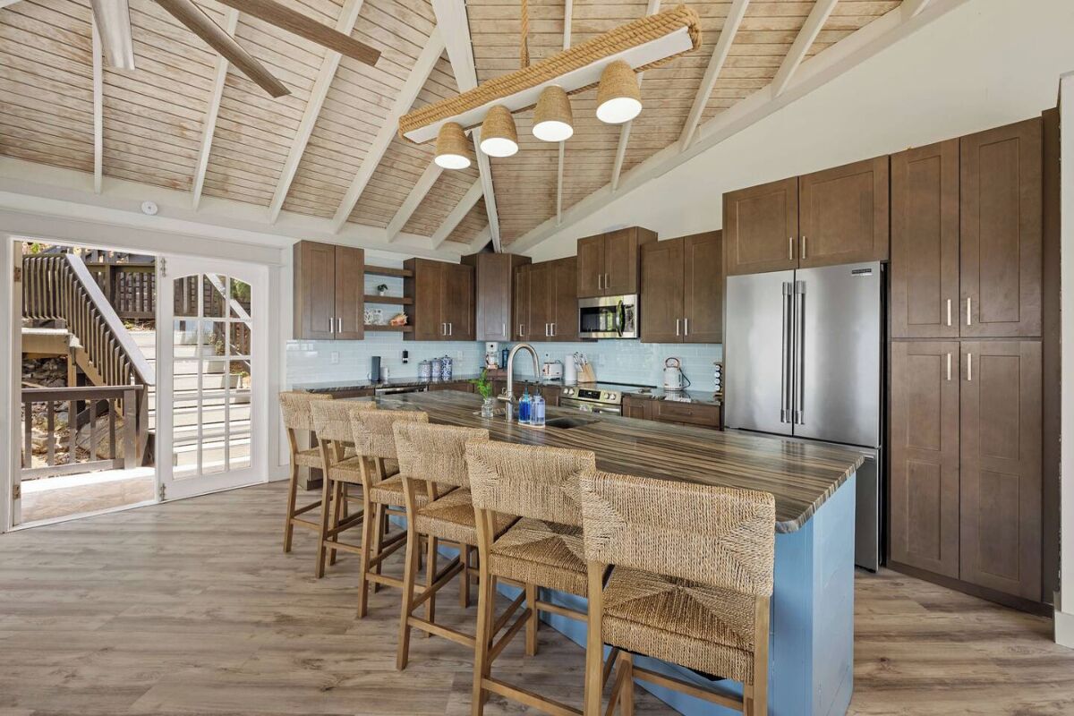 Une cuisine moderne dotée d’un grand îlot central, de tabourets de bar en bois et d’appareils électroménagers intégrés.
