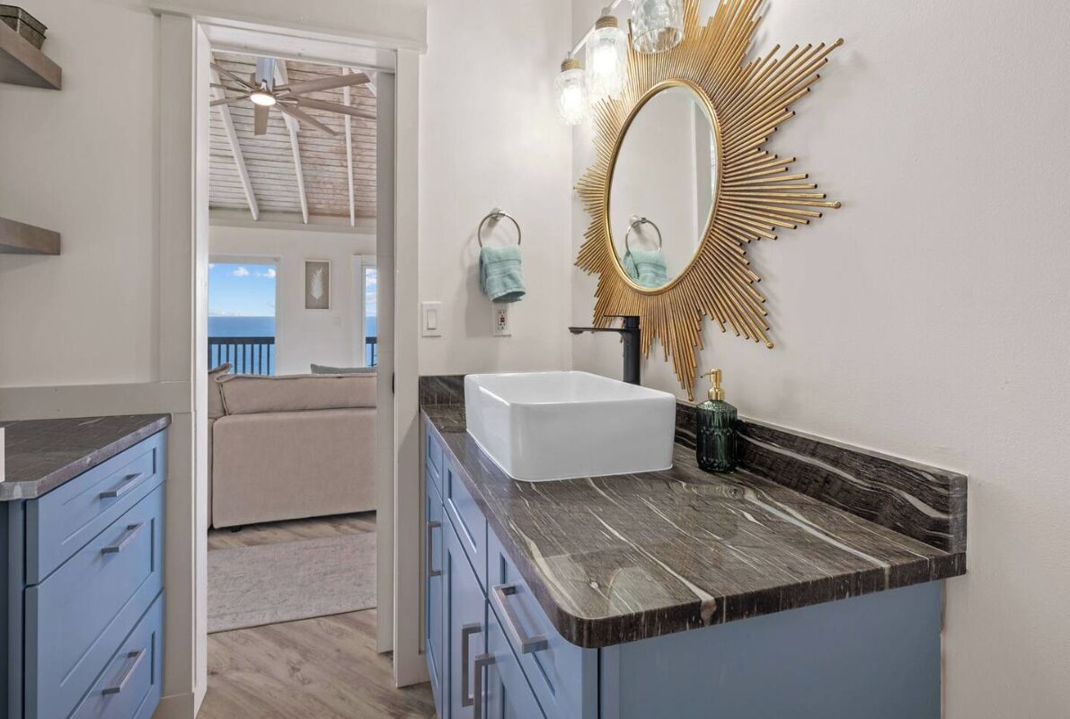 A bathroom with a white sink, a gold mirror, and a blue cabinet.