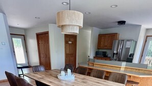 Un área de comedor moderna con una mesa y sillas de madera, una lámpara colgante y una cocina al fondo.