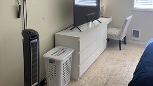A bedroom with a TV, a desk, a chair, a heater, and a laundry basket.