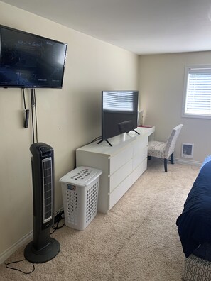 A bedroom with a TV, a desk, a chair, a heater, and a laundry basket.