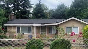A single-story house with a number '11447' on the front, a covered porch, and a fenced yard with greenery.