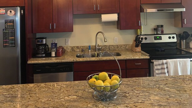 A kitchen with wooden cabinets, a stainless steel refrigerator, a coffee maker, and a bowl of lemons on the counter.