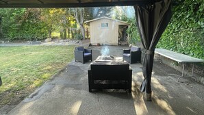 An outdoor patio area with a fire pit, seating, and a shed in the background.