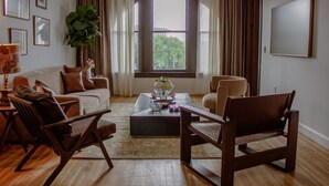 A living room with a sofa, two armchairs, a coffee table, and a large window with curtains. - The Ilium Suite 401 - Luxury 2 bd Suite in Downtown Troy (Troy)