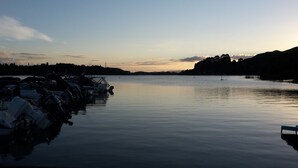 A calm lake with boats docked on the left, surrounded by hills and a clear sky.