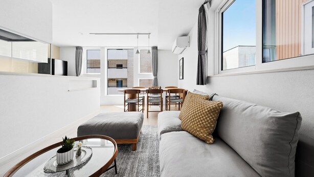 A modern living room with a sofa, ottoman, and coffee table, a dining area with chairs, and a large window. - GRACE HOME-A (Sapporo)