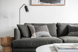 Ein modulares Sofa mit vielen Kissen, eine Stehlampe, ein Beistelltisch und ein gerahmtes Kunstwerk an der Wand.