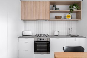 A compact kitchen with white cabinetry, a gas stove, a toaster, a coffee maker, and a sink. - The Grove  Axel apartment pet friendly (Glen Iris)