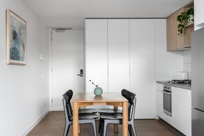 Eine moderne Küche mit weißen Schränken, einem Esstisch mit vier Stühlen und einer kleinen Pflanze auf der Arbeitsplatte.