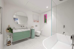 A modern bathroom with a freestanding bathtub, a green vanity, a round mirror, and a cactus decoration. - Beachside Apartment in Bondi Wellness Hub (Bondi)
