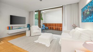 Un salon moderne doté d’un téléviseur à écran plat, de canapés blancs, d’une table basse et donnant sur une terrasse extérieure.