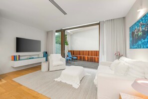 A modern living room with a flat-screen TV, white sofas, a coffee table, and a view to an outdoor deck. - Beachside Apartment in Bondi Wellness Hub (Bondi)