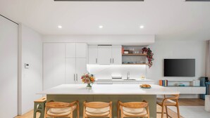 Une cuisine moderne dotée d’un îlot central, de tabourets de bar et d’un téléviseur à écran plat.