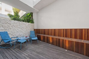 Une terrasse extérieure avec un mur en pierre, un banc en bois et des chaises bleues.