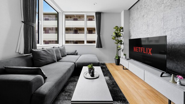 Una sala de estar moderna con un sofá seccional, una mesa de centro, un televisor de pantalla plana y un ventanal con cortinas.