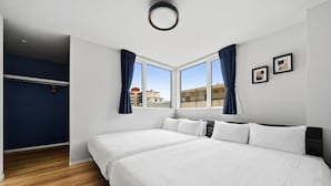 Habitación de hotel con dos camas, un ventanal con cortinas, un armario y una lámpara en el techo.