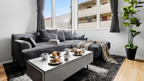 Una sala de estar moderna con un sofá gris, una mesa de centro con pasteles y una planta en maceta.