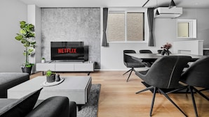 A modern living room with a flat-screen TV, grey sofa, dining table, and chairs. - GRACE HOME-B (Sapporo)